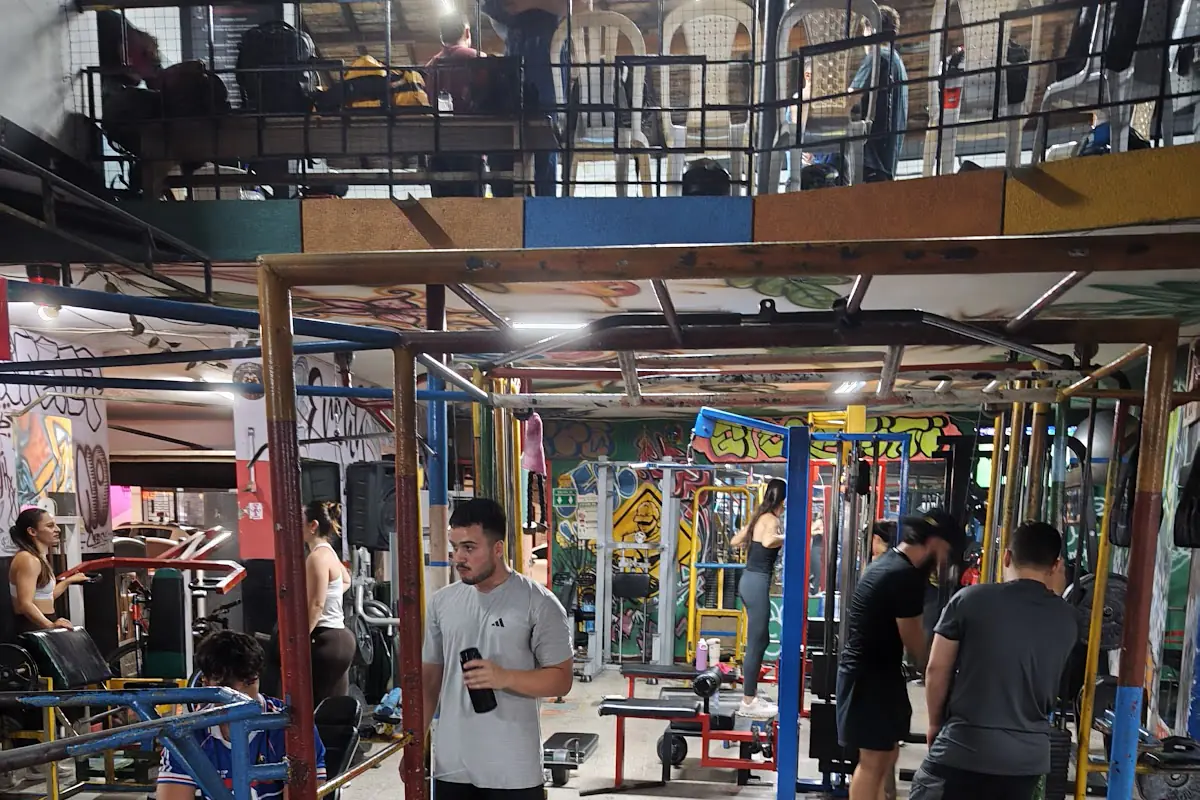 Sala de pesas de Magnum Gym con estructuras de colores, mancuernas y un segundo piso con máquinas